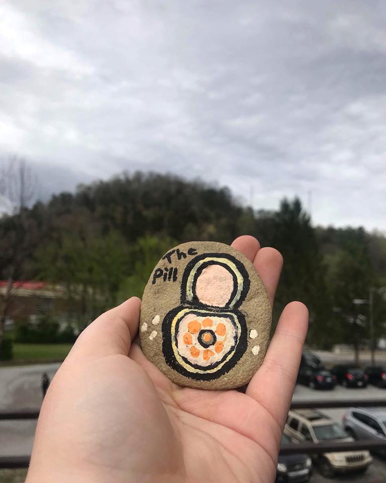 A hand holds an All Acccess EKY painted rocks focused on types of birth control. They educate about family planning in east kentucky