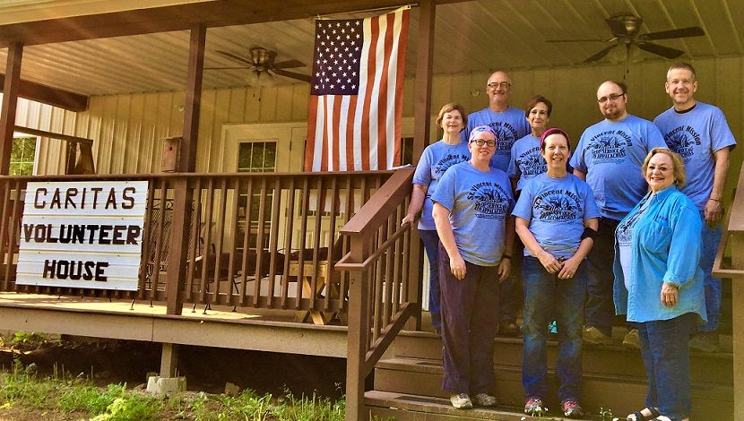 A group of people in matching shirts stand on the porch at caritas volunteer house at saint vincent mission