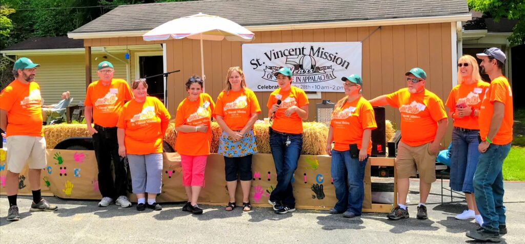 A group of people in orange matching shirts stand in front of a building at saint vincent mission