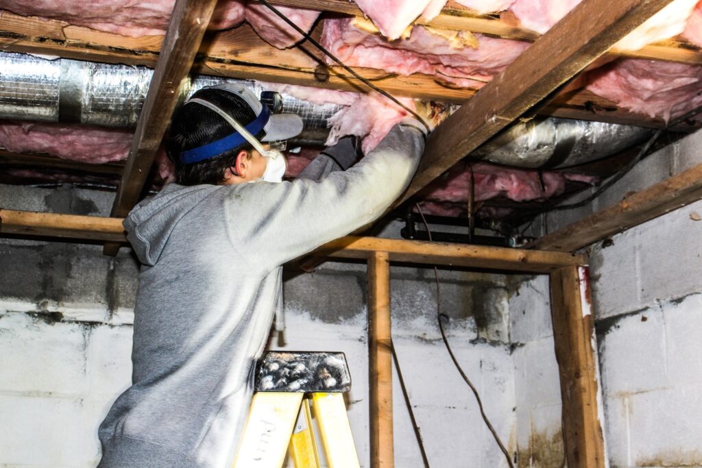 a person puts insulation in a house around duct work