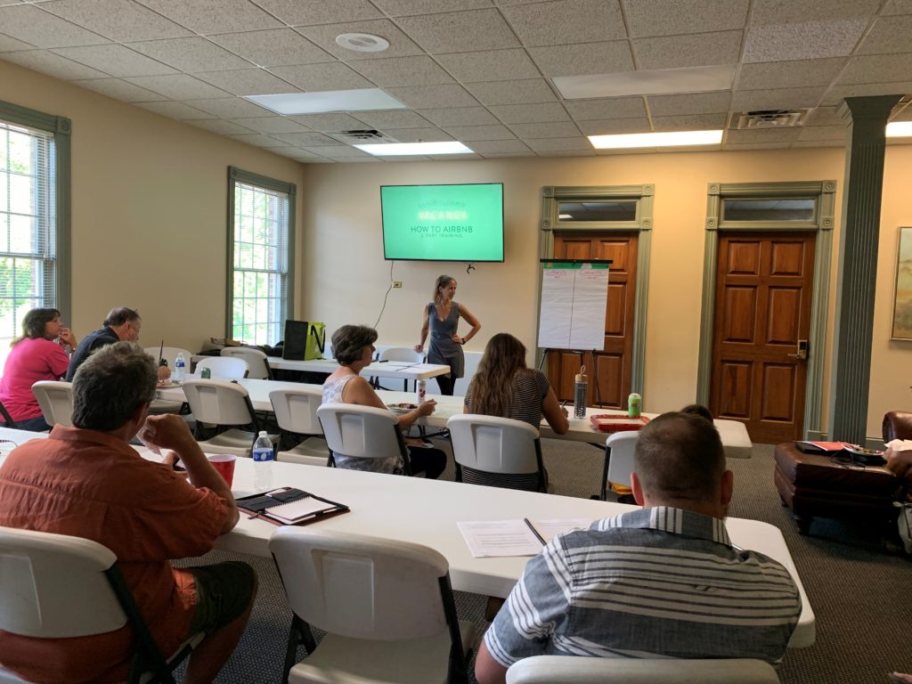 A group of participants sit in a classroom. They are being trained on how to airbnb by a MACED consultant.