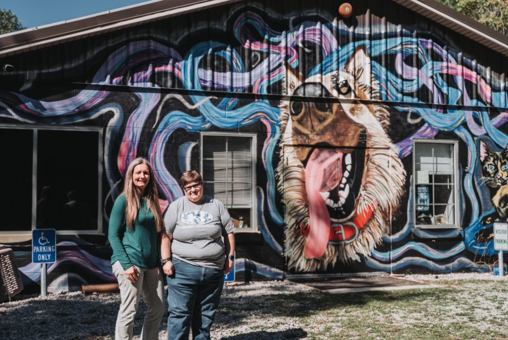 Anna and Katherine stand in front of Leslie County Animal Shelter's main building and mural