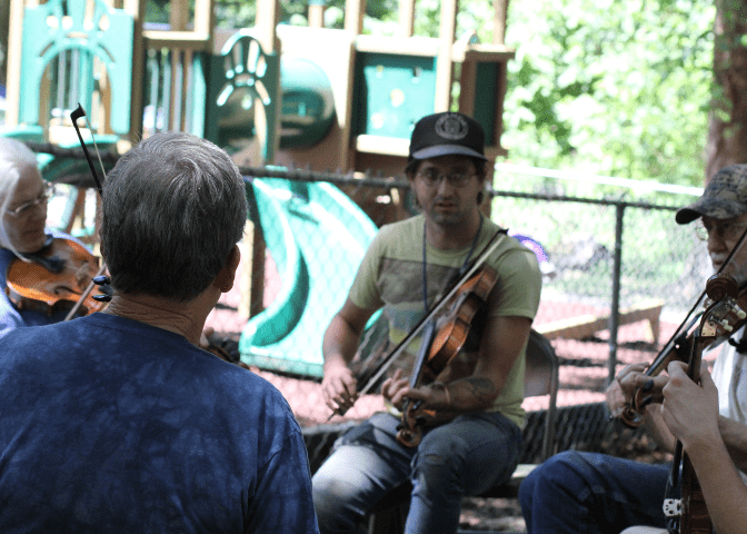 Four people sit outside playing violin at the Cowan COmmunity Center in Letcher County, kentucky while studying at Cowan Music School